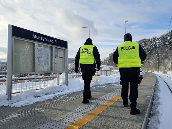 Wzdłuż torów idący strażnik ochrony kolei oraz policjant