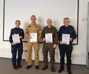 Na zdjęciu od lewej policjantka, strażak, żołnierz i strażnik miejski. Każda z osób w rękach trzyma dyplom.