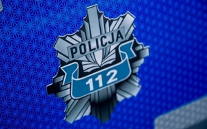 Na niebieskim tle, odznaka policyjna koloru szarego z napisem Policja 112