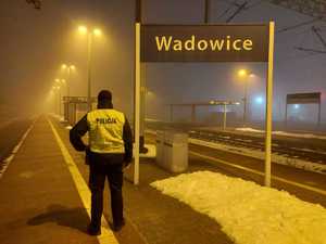 Na peronie stoi policjant tyłem w odblaskowej kamizelce z napisem Policja. Po prawej tablica z napisem Wadowice