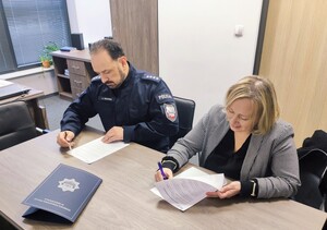 Siedzący przy stole policjant oraz kobieta w stroju cywilnym, którzy podpisują dokumenty.