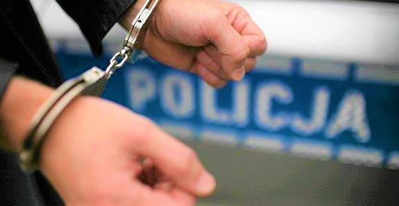 Kajdanki założone na dłonie, w tle radiowóz