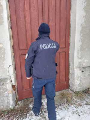 Umundurowany policjant stojący tyłem przed drewnianymi drzwiami