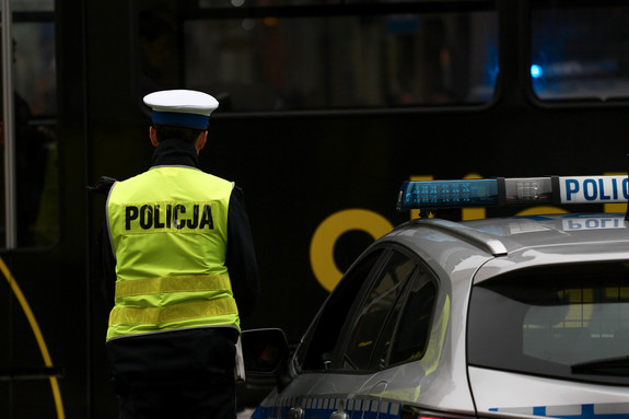 Policjant ruchu drogowego w odblaskowej kamizelce stojący tyłem, po prawej radiowóz