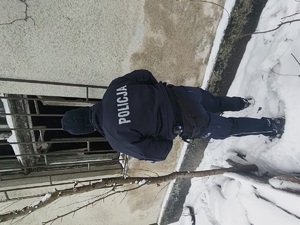 Umundurowany policjant stojący tyłem, zerkający przez okno