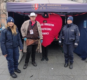 Na tle namiotu i wielkiego serca z napisem wośp dwie policjantki i mężczyzna w stroju cywilnym