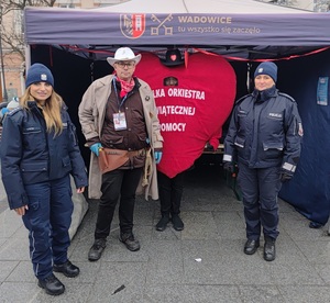 Na tle namiotu i wielkiego serca z napisem wośp dwie policjantki i mężczyzna w stroju cywilnym