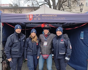 Na tle namiotu policjant, dwie policjantki i mężczyzna w stroju cywilnym