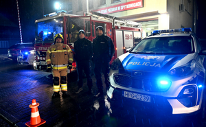 Na zdjęciu wóz strażacki oraz radiowóz i dwóch policjantów i strażak.