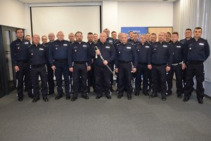 Na zdjęciu umundurowani policjanci, jeden z nich stojący pośrodku trzyma szable