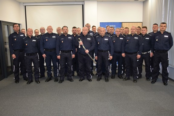 Na zdjęciu umundurowani policjanci, jeden z nich stojący pośrodku trzyma szable