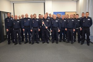 Na zdjęciu umundurowani policjanci, jeden z nich stojący pośrodku trzyma szable