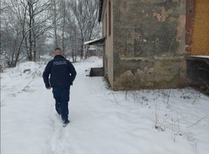 Umundurowany policjant tyłem obok pustostanu