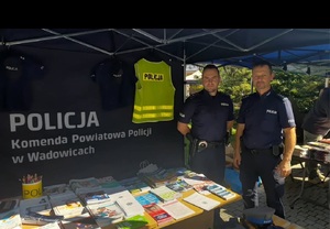 Dwóch policjantów w namiocie, gdzie na stoliku poukładane są ulotki