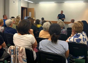 Policjant, a przed nimi osoby siedzące na krzesłach