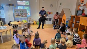 Umundurowany policjant, a przed nimi dzieci siedzące na podłodze