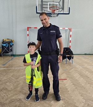 Umundurowany policjant z małym chłopcem w odblaskowej kamizelce.