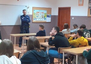 Umundurowany policjant i siedzące przed nimi dzieci w szkolnych ławkach