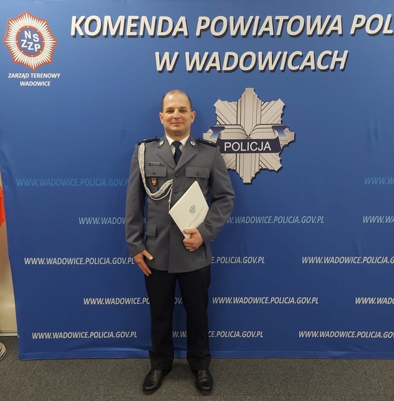 Na tle policyjnego baneru policjant w mundurze galowym