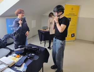 Chłopak przymierzający kask policyjny obok stoi policjantka