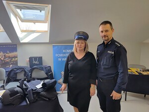 Kobieta w czapce policyjnej obok niej umundurowany policjant