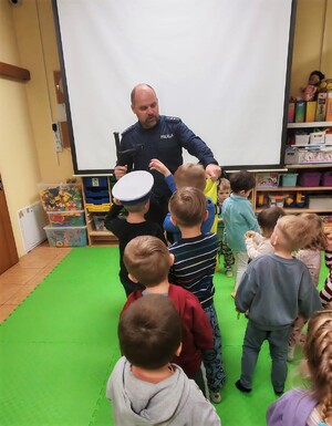 Policjant, a przed nim dzieci mierzące elementy umundurowania policyjnego