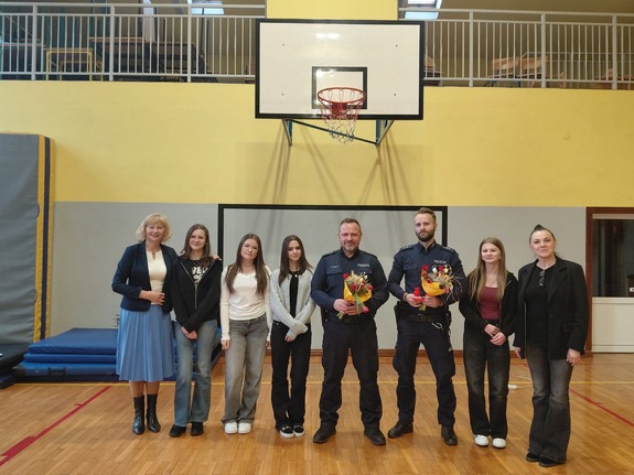 Sześć kobiet w stroju cywilnym oraz dwóch policjantów z kwiatami w ręku