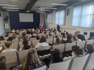 Na auli siedzą uczniowie, po prawej stronie policjant