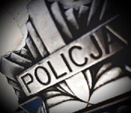 Fragment odznaki policyjnej koloru szarego z napisem Policja.