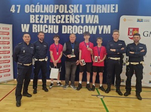Na tle banerów czterech policjantów oraz trzech chłopaków z medalami  na szyi. Pośrodku mężczyzna w stroju cywilnym.