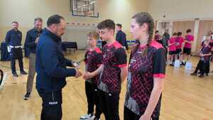 Policjant wręczający statuetkę dwóm chłopakom i dziewczynie. W tle osoby.