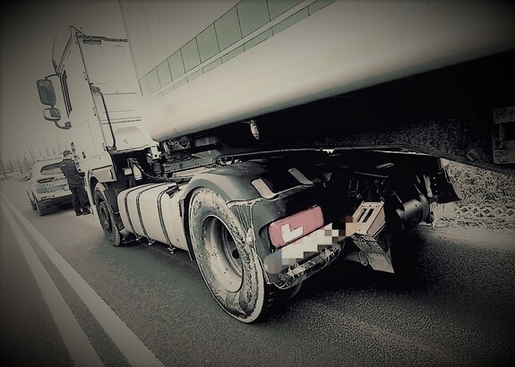 Samochód ciężarowy, a przed nim radiowóz i policjant.
