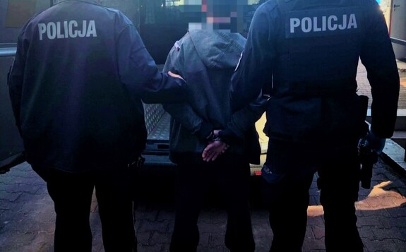 Dwóch policjantów, a pośrodku zatrzymany mężczyzna.  Osoby są tyłem.