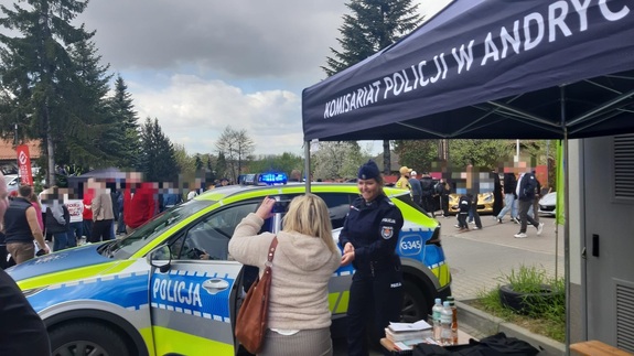 Na tle namiotu i radiowozu policjantka oraz kobieta. W tle tłum osób.