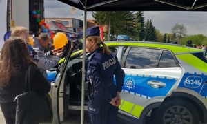 Policjantka i oznakowany radiowóz. W tle grupa osób.