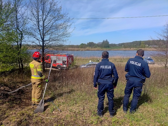 Dwóch policjantów i strażak oraz radiowozy i wóz strażacki