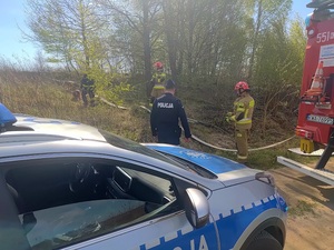 Radiowóz i wóz strażacki. W tle strażacy i policjanci