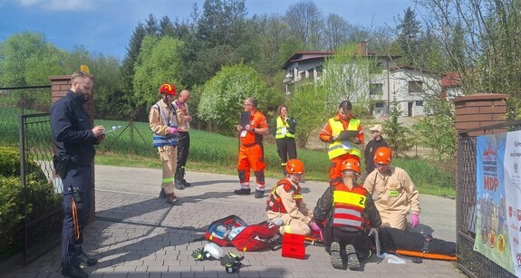 Scenka z poszkodowaną osobą. Nadzoruje policjant, przedstawiciel medyczny i strażak