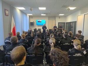 Dwóch policjantów i policjantka oraz grupa uczniów siedzących przed nimi na krzesłach.