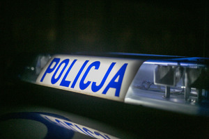 Na białym tle niebieski napis Policja, po prawej i lewej stronie światła