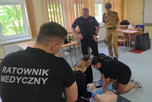 Na zdjęciu policjant, strażak, ratownik medyczny i cztery osoby ćwiczące na manekinie