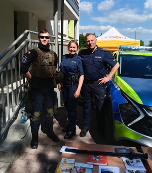 Obok radiowozu policjant, policjantka oraz uczeń klasy mundurowej