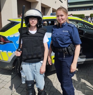 Na tle radiowozu policjantka i chłopak ubrany w elementy wyposażenia policyjnego