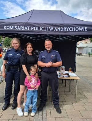 Na tle  policyjnego namiotu policjantka, policjant oraz kobieta z małą dziewczynką