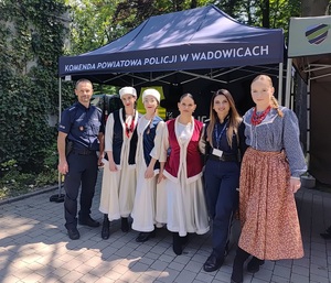 Na tle namiotu cztery uczennice ubrane w stroje ludowe oraz policjant i policjantka.
