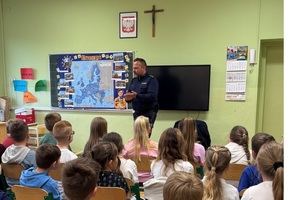 Dzieci siedzące na krzesłach, przed nimi stoi policjant