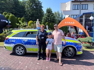 policjantk pozuje do zdjęcia z uczestnikami pikniku na tle radiowozu