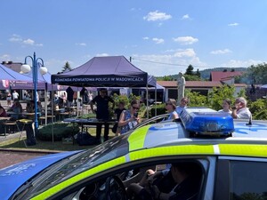 stoisko policyjne podczas pikniku, na stoisku umundurowany policjant, na pierwszym planie radiowóz