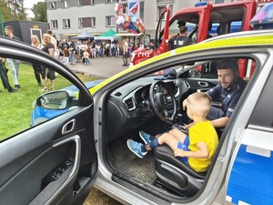 chłopiec siedzi za kiernicą oznakowanego radiowozu, obok policjant