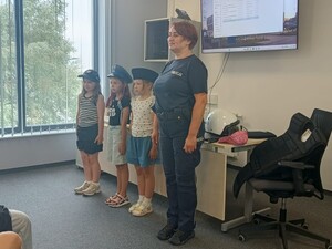 policjantk ćwiczy musztrę z dziećmi, które maja założone na głowach rózne czapki policyjne, musztra odbywa sie na sali sztabowej komendy
